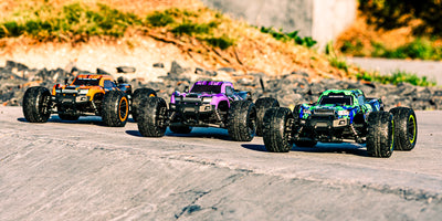 Tre farverige Hunter MT10 fjernstyrede monster trucks vist sammen i et bakket udendørs terræn.