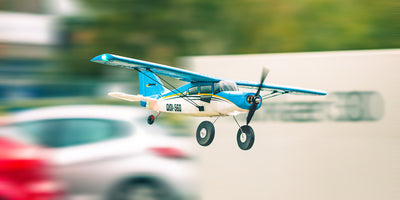 Hvidt og blåt QIDI-560 Sports Flyer fjernstyret fly med brushless motor i luften over en grøn mark.