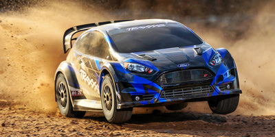 Blå Traxxas Ford Fiesta ST Rally brushless fjernstyret bil med offroad dæk vist på hvid baggrund.