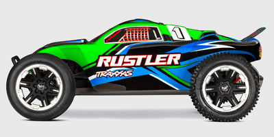 Blå Traxxas Rustler 2WD fjernstyret bil set skråt forfra med detaljerede offroad-dæk på hvid baggrund.
