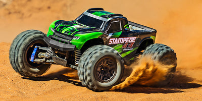 Blå Traxxas Stampede 4x4 BL-2S monster truck kører gennem vandpytter og sprøjter med mudder i terrænet.